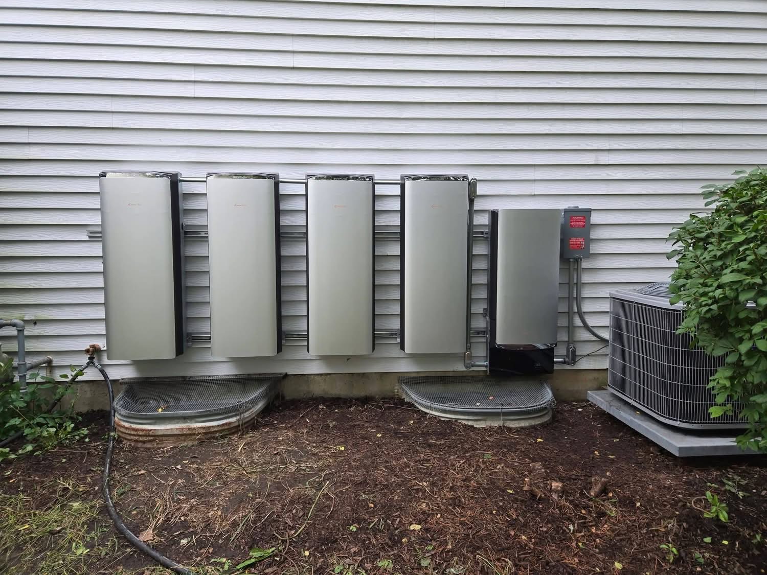 Home battery backup system with four units installed on a home's white siding, next to the air conditioning unit